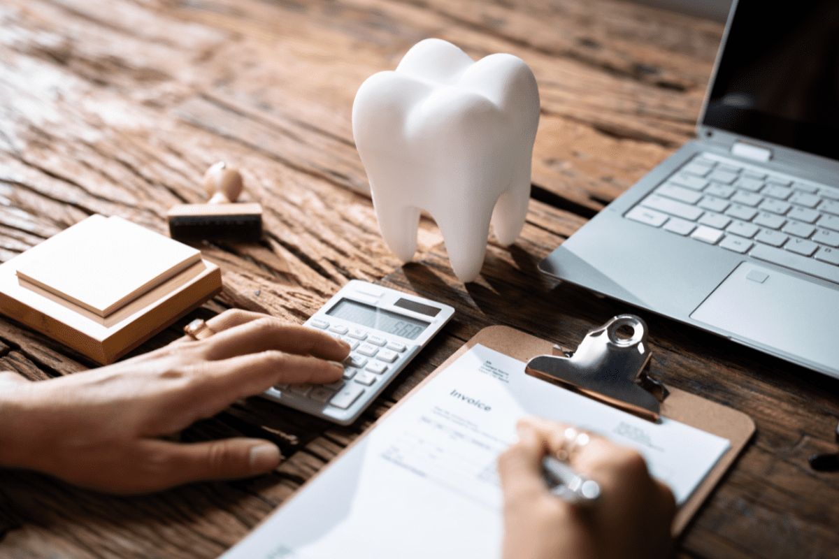 Person performing financial work on a clipboard and calculator with a tooth sculpture implying a dental office.